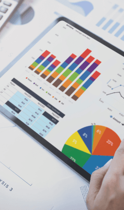 Das Bild zeigt eine Person, die ein Tablet benutzt, auf dem Diagramme und Grafiken angezeigt werden. Die Datenvisualisierungen umfassen Balkendiagramme, Kreisdiagramme und Liniendiagramme, die möglicherweise Finanzdaten, Strategien oder Unternehmenskennzahlen darstellen. Das Bild vermittelt einen geschäftlichen Kontext, in dem die Analyse und Auswertung von Daten im Vordergrund stehen, um Entscheidungen zu treffen oder Trends zu beobachten. Es zeigt eine professionelle Arbeitsumgebung.