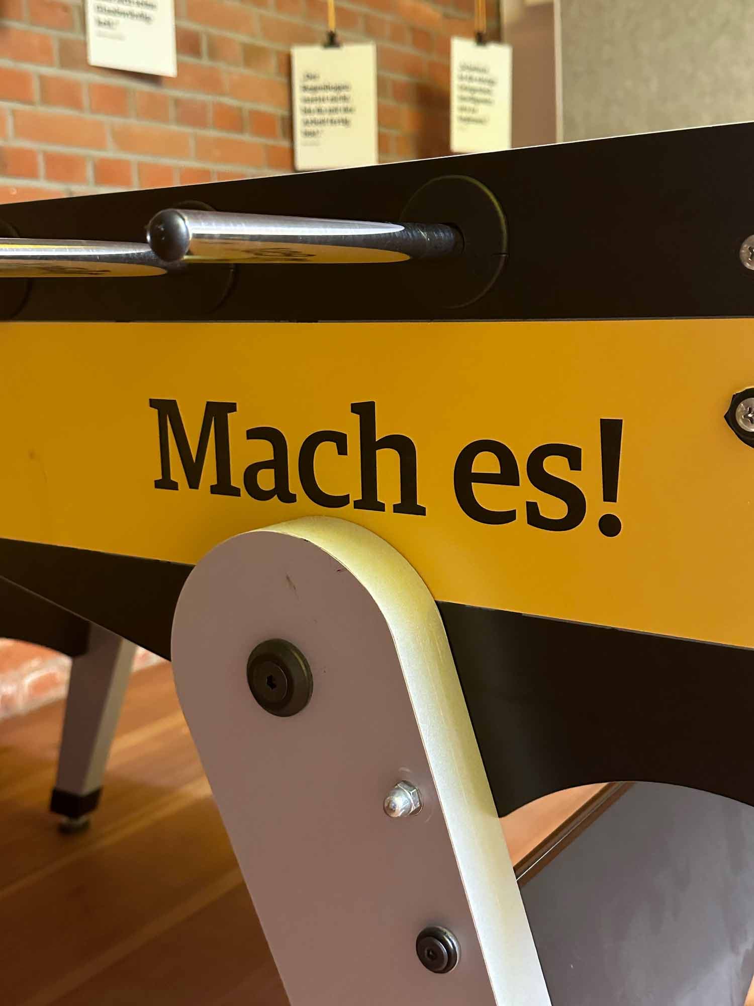 Auf einem Abschnitt eines Billiardtisches ist das Motto des MachWerks "Mach es!" abgebildet 